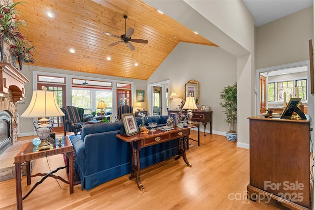 living area featuring ceiling fan, high vaulted ceiling, baseboards, a glass covered fireplace, and light wood-type flooring