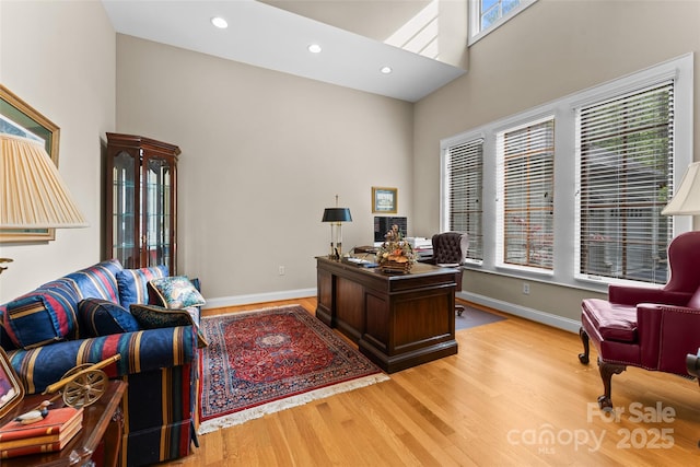office space featuring a towering ceiling, wood finished floors, baseboards, and recessed lighting
