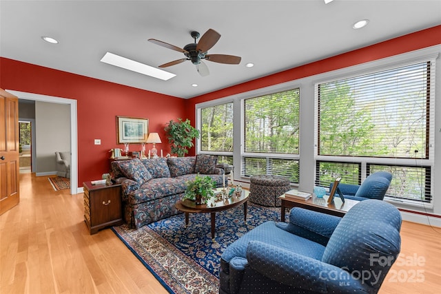 living area featuring a ceiling fan, light wood-style floors, a skylight, recessed lighting, and baseboards