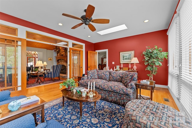 living area featuring wood finished floors, a ceiling fan, a skylight, recessed lighting, and baseboards