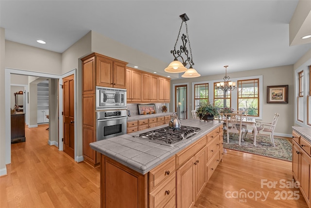 kitchen featuring stainless steel appliances, tile counters, light wood-type flooring, a kitchen island, and recessed lighting