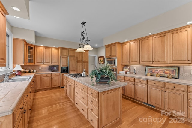 kitchen featuring tile countertops, a sink, a center island, light wood-style flooring, and tasteful backsplash