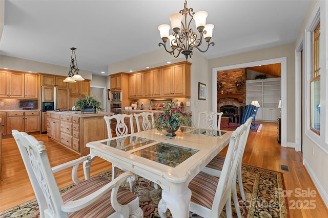 dining room with light wood finished floors, a chandelier, recessed lighting, a fireplace, and baseboards
