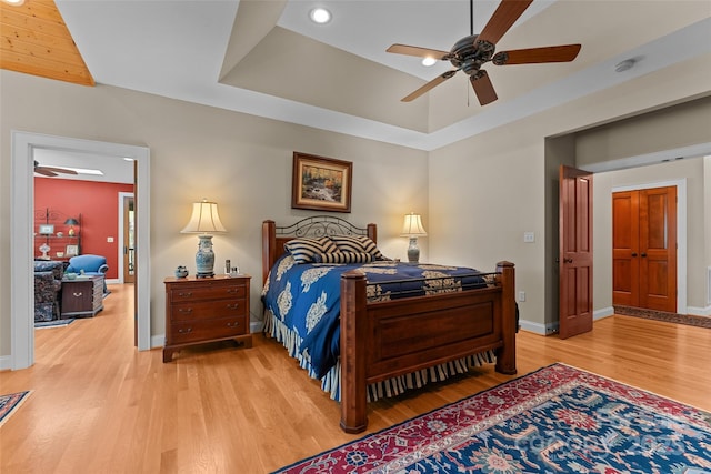 bedroom featuring light wood-style floors, baseboards, recessed lighting, a raised ceiling, and ceiling fan
