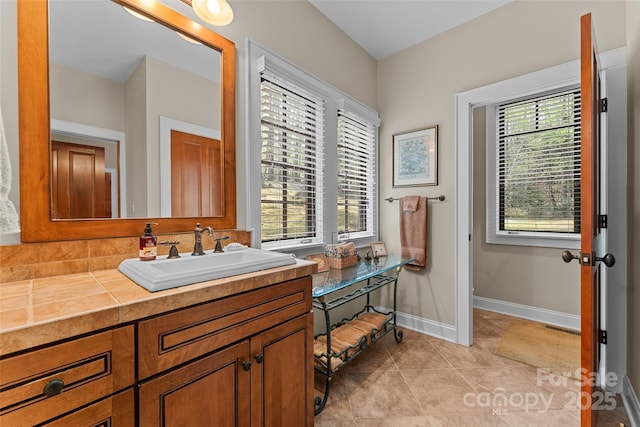bathroom with healthy amount of natural light, baseboards, tile patterned floors, and vanity