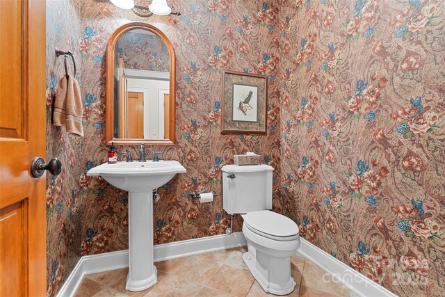half bathroom featuring baseboards, tile patterned flooring, toilet, and wallpapered walls