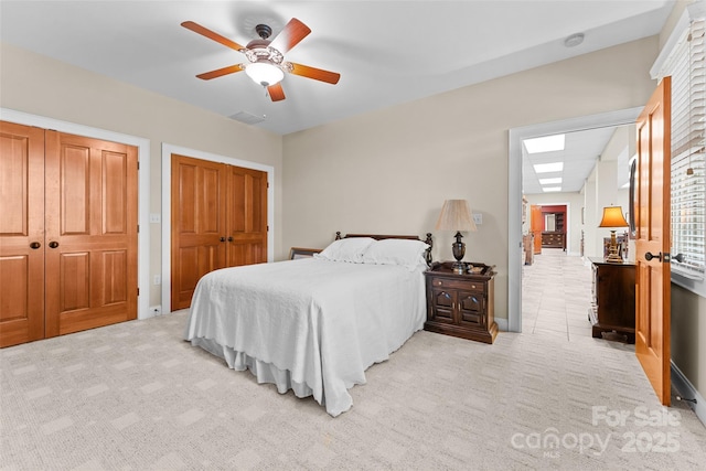 bedroom with light colored carpet, multiple closets, ceiling fan, and baseboards