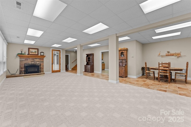 carpeted living room with a fireplace, tile patterned floors, baseboards, a drop ceiling, and stairway