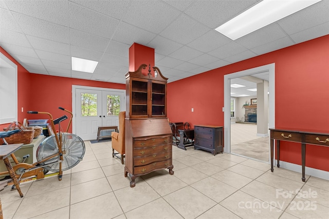 office area with a paneled ceiling, french doors, light tile patterned floors, and a stone fireplace