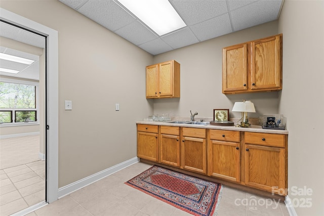 kitchen with a sink, light countertops, baseboards, a paneled ceiling, and light tile patterned flooring