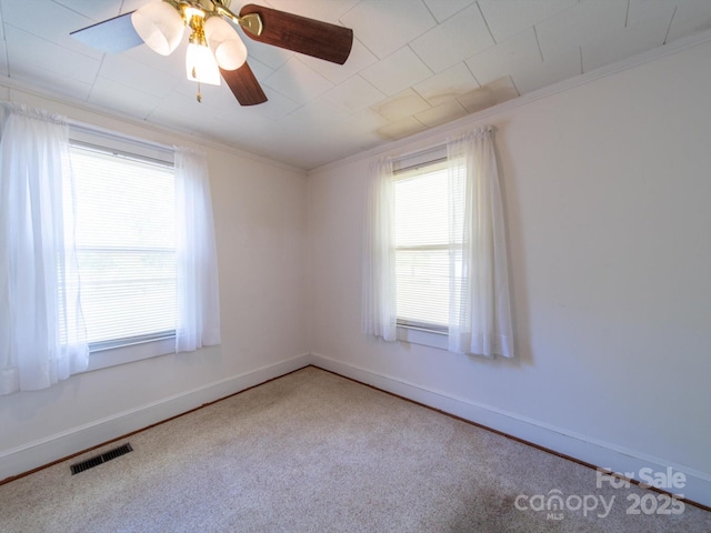 carpeted spare room featuring baseboards, ceiling fan, ornamental molding, and visible vents