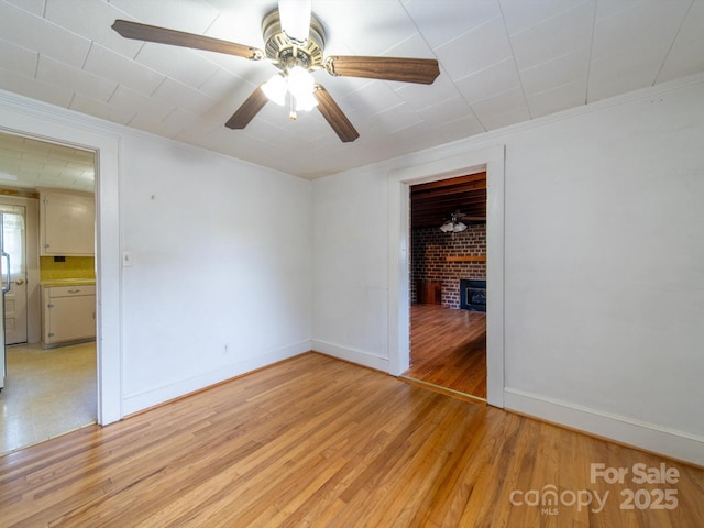 unfurnished room with light wood-style flooring, a brick fireplace, baseboards, and a ceiling fan