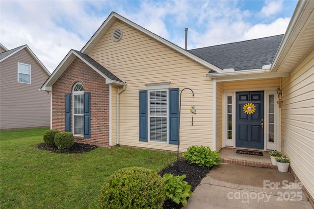 entrance to property featuring a lawn, brick siding, and roof with shingles