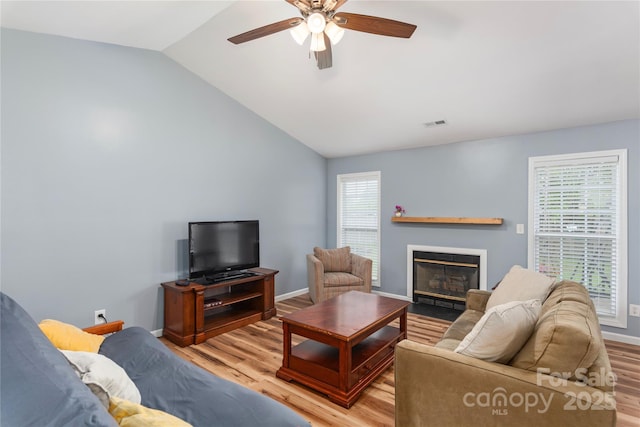 living area featuring ceiling fan, a fireplace with flush hearth, light wood-style flooring, lofted ceiling, and healthy amount of natural light