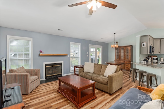 living room with light wood-type flooring, ceiling fan, lofted ceiling, a fireplace with flush hearth, and a chandelier