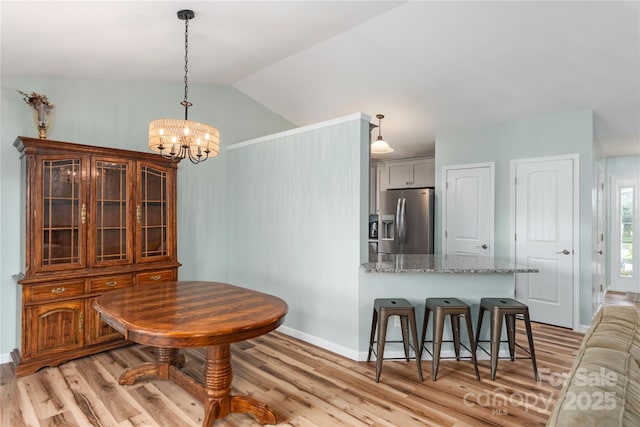 dining space featuring light wood-style flooring, a chandelier, baseboards, and vaulted ceiling