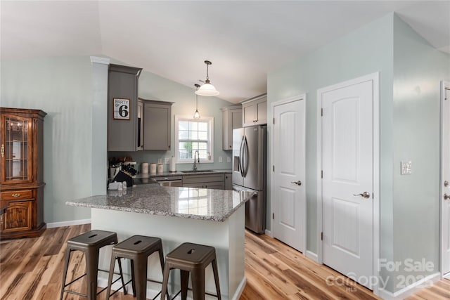 kitchen with appliances with stainless steel finishes, gray cabinetry, a sink, a breakfast bar, and light stone counters