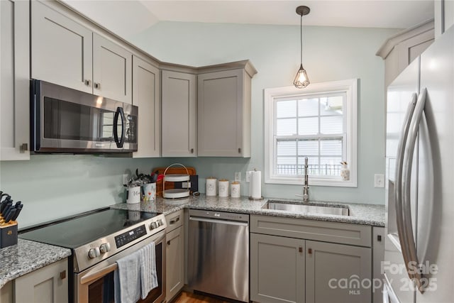 kitchen featuring stainless steel appliances, a sink, gray cabinetry, decorative light fixtures, and light stone countertops