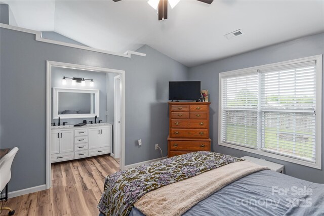 bedroom featuring lofted ceiling, light wood finished floors, a sink, ensuite bathroom, and baseboards