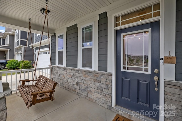 doorway to property with a porch, stone siding, and concrete driveway