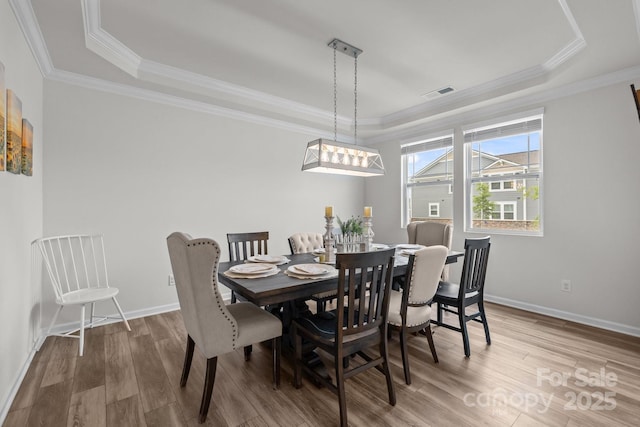 dining area featuring a raised ceiling, wood finished floors, baseboards, and crown molding