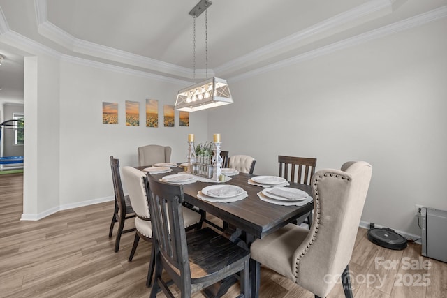 dining room with wood finished floors, a tray ceiling, baseboards, and ornamental molding