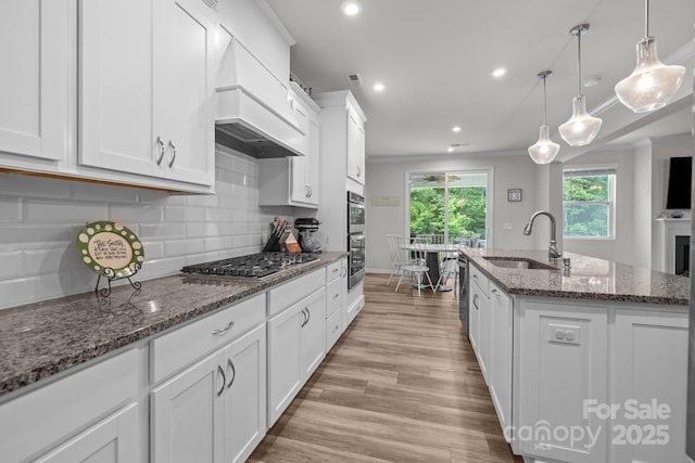 kitchen featuring a sink, appliances with stainless steel finishes, custom range hood, ornamental molding, and white cabinets