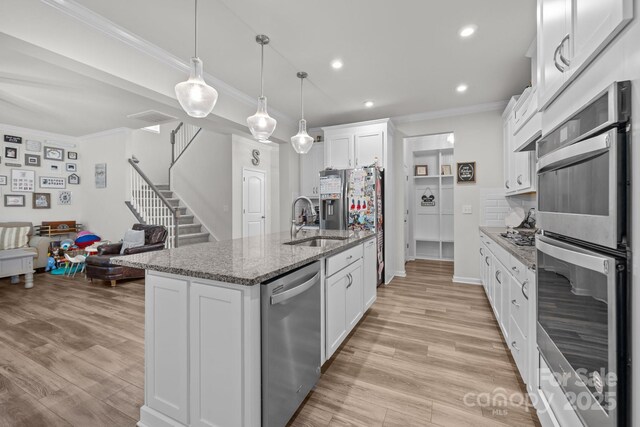 kitchen with stainless steel appliances, a sink, crown molding, white cabinetry, and stone counters