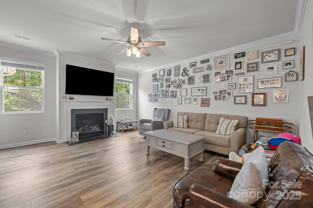 living area with crown molding, ceiling fan, light wood-style flooring, a fireplace with flush hearth, and baseboards