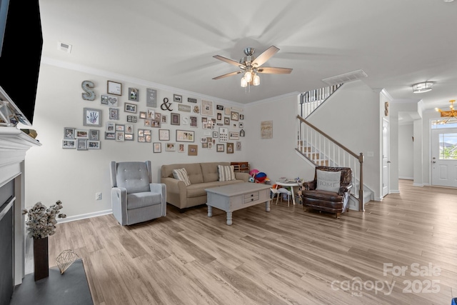 living area featuring crown molding, stairway, light wood-style flooring, a fireplace with flush hearth, and ceiling fan