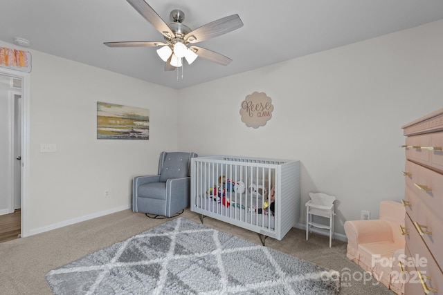 carpeted bedroom featuring a nursery area, baseboards, and a ceiling fan