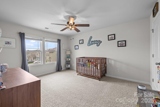 carpeted bedroom with baseboards, a nursery area, and a ceiling fan