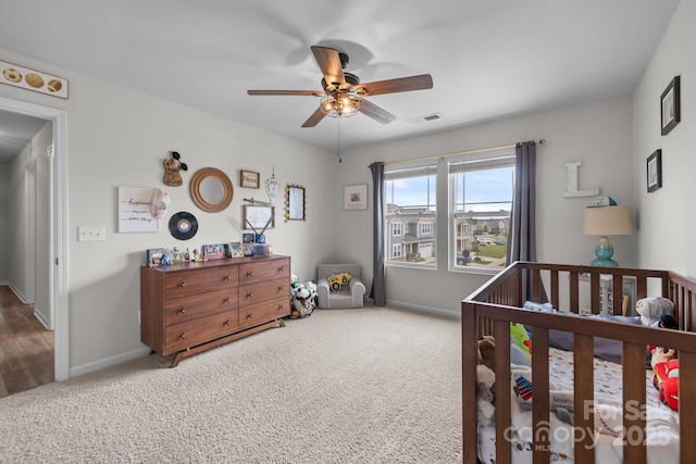 carpeted bedroom with a crib, baseboards, and ceiling fan