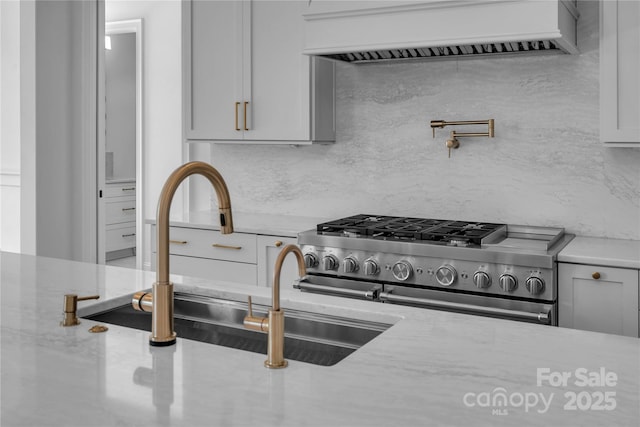 kitchen featuring light stone counters, a sink, high end stainless steel range, ventilation hood, and decorative backsplash