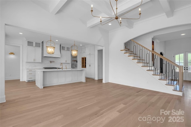 unfurnished living room featuring light wood finished floors, beam ceiling, a chandelier, and stairs