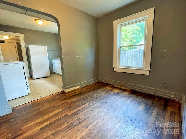 empty room featuring arched walkways, baseboards, and light wood-style floors