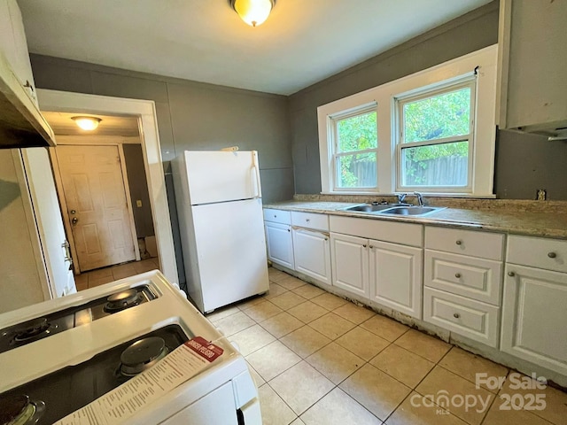 kitchen featuring a sink, freestanding refrigerator, light tile patterned flooring, white cabinetry, and range