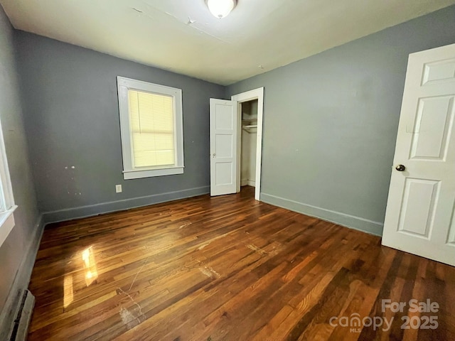 unfurnished bedroom with a baseboard heating unit, baseboards, a closet, and wood finished floors