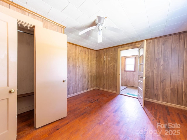 1470 Hilltop St, Albemarle, NC 28001 - unfurnished bedroom with baseboards, wooden walls, a ceiling fan, and wood finished floors