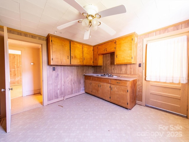 1470 Hilltop St, Albemarle, NC 28001 - kitchen with brown cabinetry, light floors, wood walls, baseboards, and ceiling fan