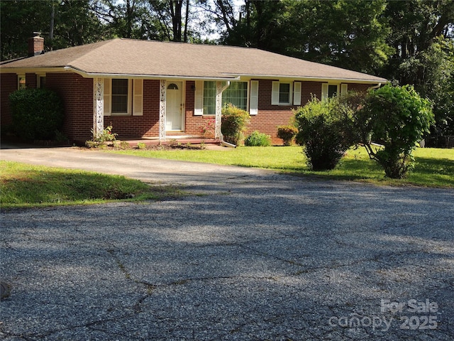 single story home with a chimney, driveway, brick siding, a front yard, and a porch