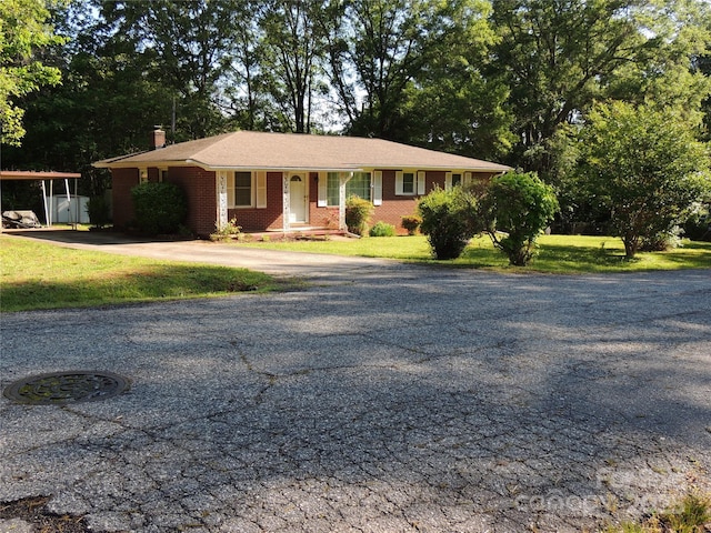 ranch-style home featuring a chimney, a front yard, brick siding, and aphalt driveway