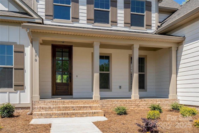 view of exterior entry featuring board and batten siding, a shingled roof, and covered porch
