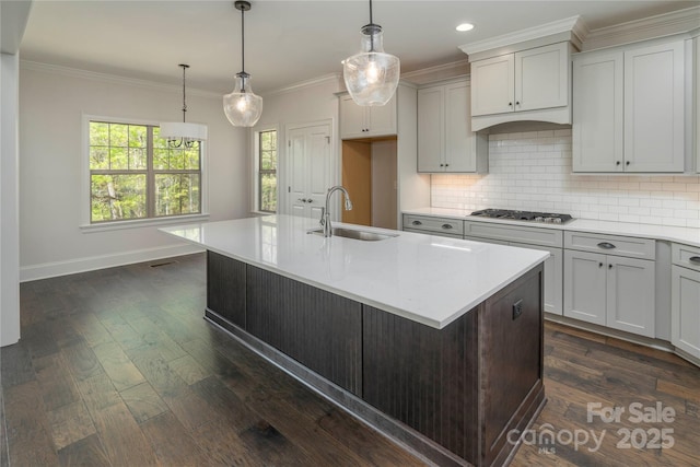 kitchen featuring light countertops, stainless steel gas stovetop, crown molding, and a sink