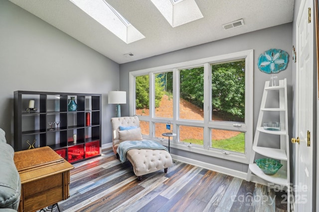 living area with wood finished floors, vaulted ceiling with skylight, a textured ceiling, visible vents, and baseboards