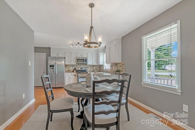 dining room with a chandelier, light wood-style flooring, and baseboards