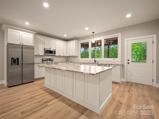 109 Ashley Ct, Mill Spring, NC 28756 - kitchen with stainless steel appliances, a center island, light wood-style flooring, white cabinets, and backsplash