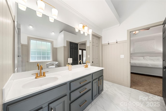 ensuite bathroom with double vanity, wainscoting, a decorative wall, and ornamental molding