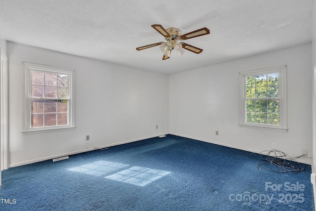 spare room with dark carpet, a textured ceiling, visible vents, baseboards, and ceiling fan
