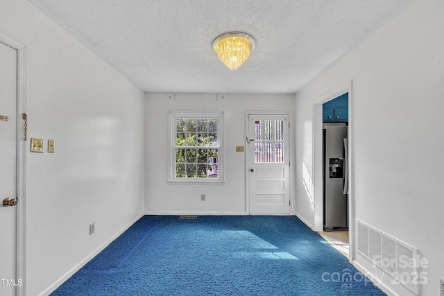 carpeted entrance foyer with baseboards, an inviting chandelier, visible vents, and a textured ceiling